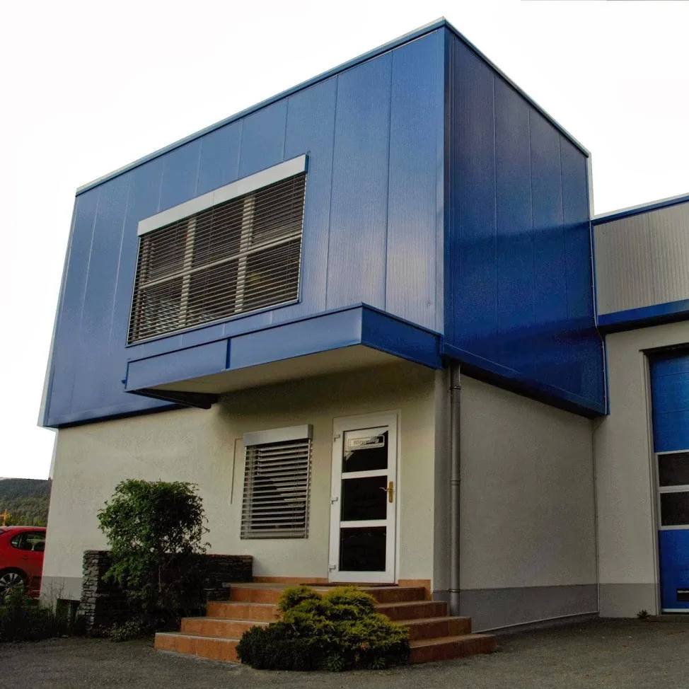 Eingang des Bürotrakts mit blauer Paneelfassade und Treppe