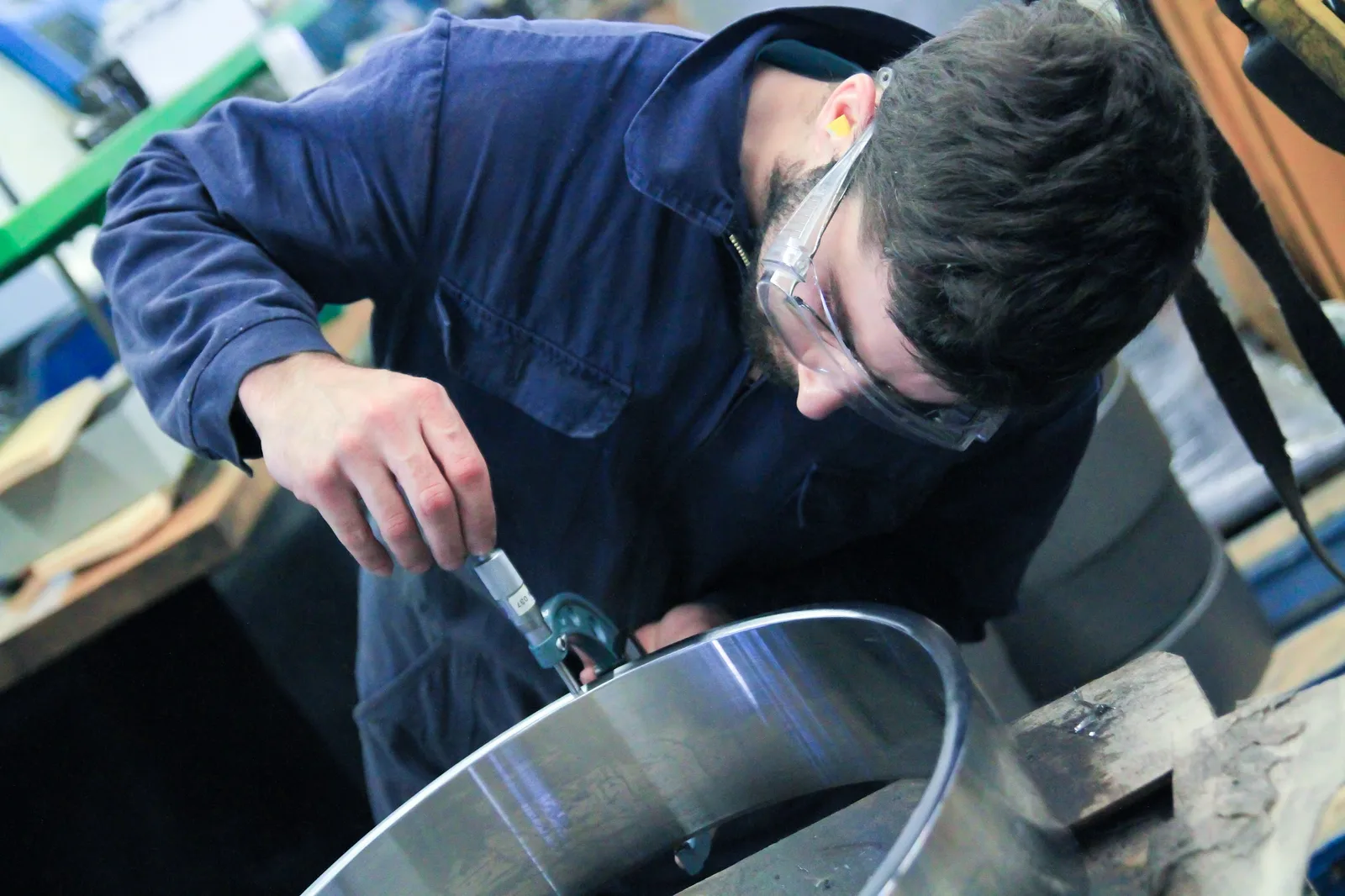 Mitarbeiter mit Schutzbrille misst mit einer Bügelmessschraube an einem gedrehten Metallring